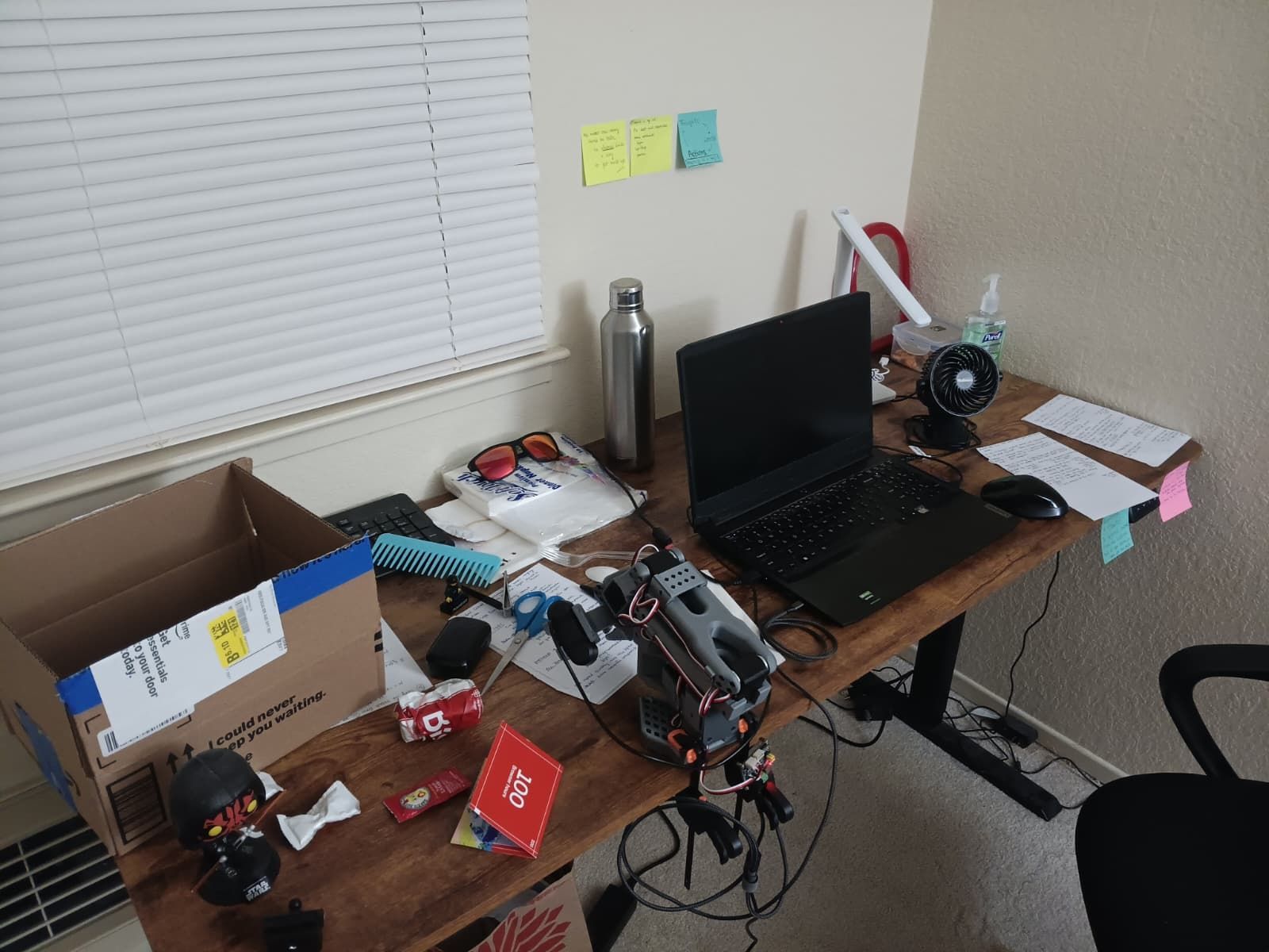Hitesh's cluttered desk: an open box, a crushed can, scissors, a comb, snacks and papers around an SO-101 robot arm